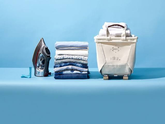 A neat stack of folded clothes beside an iron and laundry bag